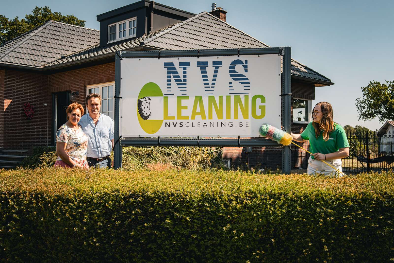 Medewerkster van NVS Cleaning voor een woning, naast het bord van het bedrijf